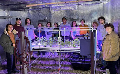 students posing with aquaponics plants growing under lights