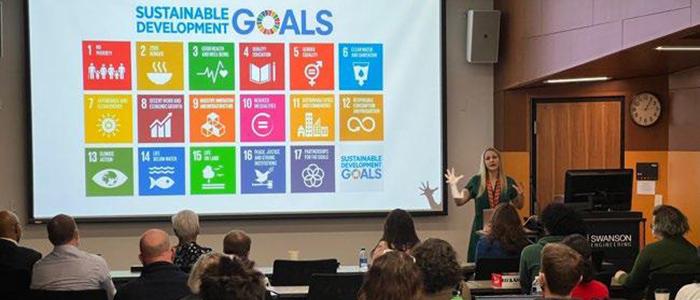 woman presenting Sustainable Development Goals slide before a gathered audience