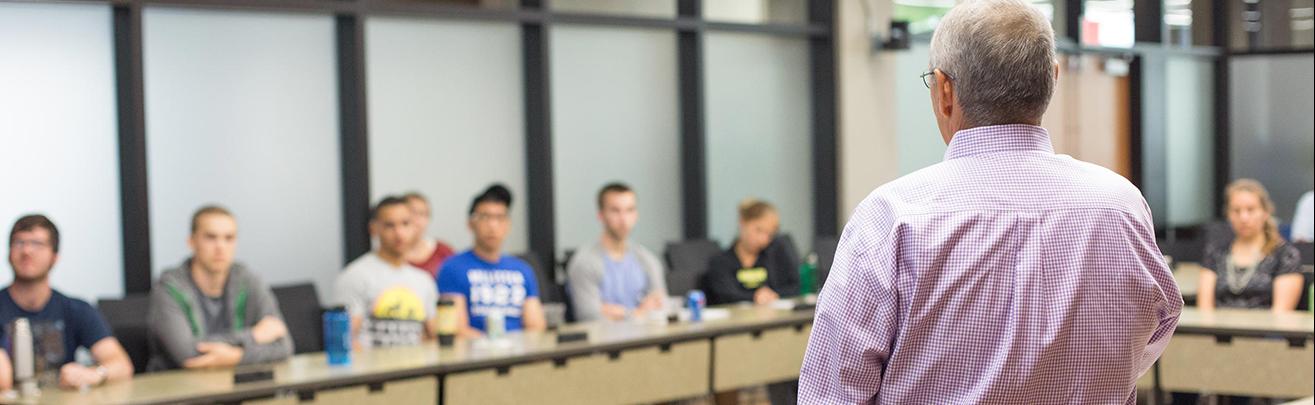 instructor talking to students sitting at desks